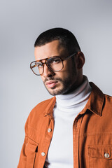Trendy man in eyeglasses and terracotta jacket looking at camera isolated on grey