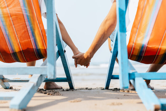 Couple of lovers sitting on beach chair holding hands on the beach in the morning.  Newlywed couple on a romantic vacation