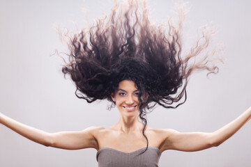 Beautiful brunette girl with long curly hair in the air, studio portrait. Happy smiling face...
