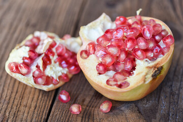 Pomegranate fruit and cut half ripe pomegranate with seeds on wooden table background.