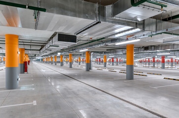 Large underground parking for cars, columns are painted red and orange.