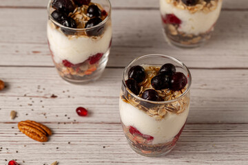 Angled view of delicious fruit yogurt parfait  cups filled with layers of muesli, chia seeds, fresh berries, rolled oats, and homemade yogurt served with pomegranate and pecan on wooden background.