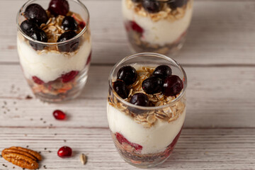 Angled view of delicious fruit yogurt parfait  cups filled with layers of muesli, chia seeds, fresh berries, rolled oats, and homemade yogurt served with pomegranate and pecan on wooden background.