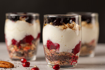 Side view of Delicious fruit and yogurt parfait  cups filled with layers of muesli, chia seeds, fresh berries, rolled oats, and homemade yogurt served with pomegranate and pecan on wooden background.