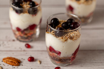 Angled view of delicious fruit yogurt parfait  cups filled with layers of muesli, chia seeds, fresh berries, rolled oats, and homemade yogurt served with pomegranate and pecan on wooden background.