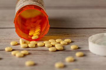 An orange prescription medication bottle tipped over on wooden table with round yellow pills...