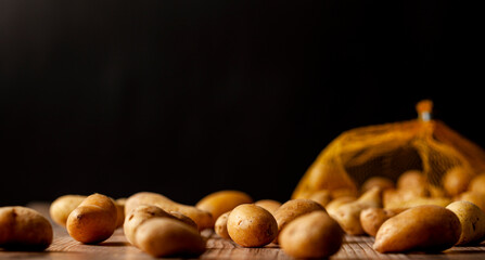 Shallow depth of field dark image of small irregular shaped ratte potatoes scattered on the surface of a wooden table from a tipped over mesh sack. An artistic versatile low light still life photo.