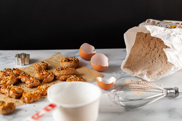 View of fresh out of oven handmade cookies and biscuits made with wholewheat flour, egg and decorated with sesame and poppy seeds. They are on baking paper cooling over marble with ingredients around.