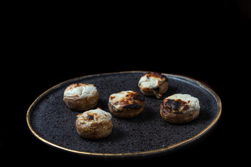 top view of stuffed mushrooms on a plate with black texture and golden edges.