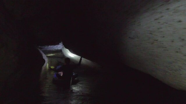 Adventurous tourists kayak in tight, dark, claustrophobic cave underground in Thailand for exotic adventure travel. Prores file, shot in 4K UHD.