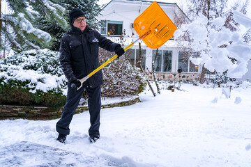 An elderly European, 61, throws snow with an orange shovel while clearing a path outside his home....