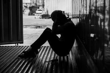 Depressed and tried foreman or business man sitting in side container in shipyard logistic factory because losing his job or fired. Worker or officer sad.