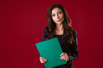A woman director is holding documents and smiling on a red background.