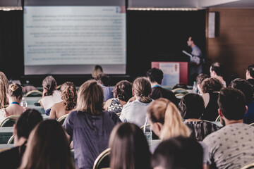 Speaker Giving a Talk at Business Meeting. Audience in the conference hall. Business and Entrepreneurship. Focus on unrecognizable people from rear.