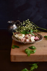 A bowl of feta cheese with herbs on a wooden table over a black background.