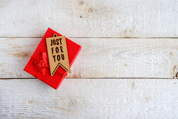 Red gift box on white wooden background. Tag with text just for you