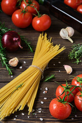 Whole grain spaghetti with ingredients for cooking Italian style lunch on a dark wooden table. The idea of cooking pasta. Close-up, selective focus