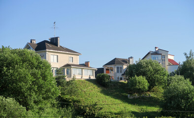 Fototapeta na wymiar Village, country houses, SNT on a hill with green grass to the horizon. Close-up of one-and two-storey houses with a lawn and fresh spring grass in the foreground. The horizontal landscape.