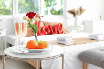 Glasses of champagne, fruits and flowers on table in hotel honeymoon room