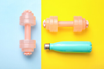 Stylish dumbbells and bottle of water on color background