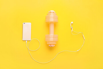 Stylish dumbbell, earphones and mobile phone on color background