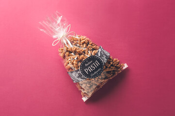 Bag with uncooked pasta on color background