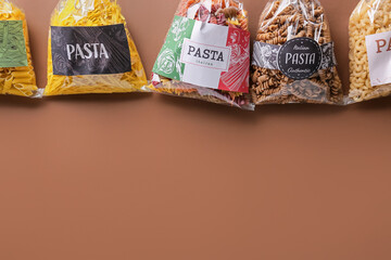 Bags with uncooked pasta on color background