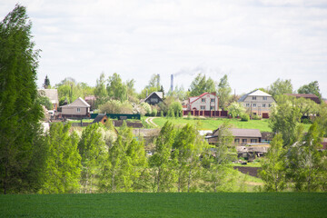 A lawn with green grass all the way to the horizon. Horizontal landscape of a flat field with fresh spring grass. Village, country houses, SNT, on the background of fields and trees.
