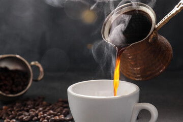 Pouring hot coffee from cezve in cup on dark background