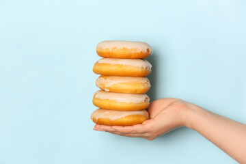 Female hand with tasty donuts on color background