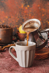 Pouring coffee from cezve in cup on table