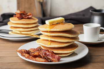 Plates of tasty pancakes with fried bacon and butter on wooden table