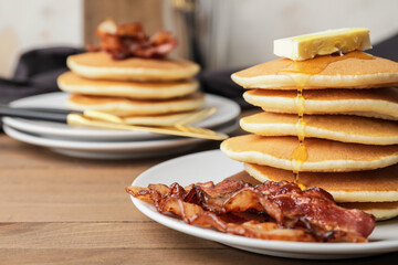 Plates of tasty pancakes with fried bacon and butter on wooden table