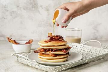 Woman pouring honey onto tasty pancakes with fried bacon on table