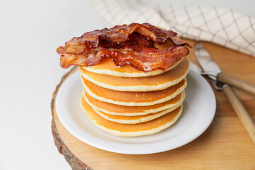 Plate of tasty pancakes with fried bacon on table