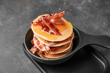 Frying pan of tasty pancakes with fried bacon on table