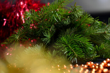 Winter background with branches of a Christmas tree close-up, the needles and the trunk. Orange beads in the foreground are blurred, yellow lights. New Year's and Christmas.