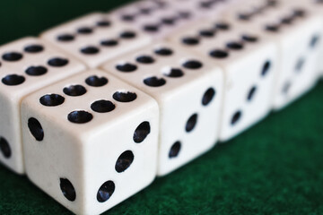 A close up image of several black and white dice lined up in a row on dark green felt cloth. 