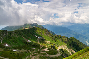 Landscape of green valley, forested mountains and a bit of snow on a grass