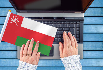 woman hands and flag of Oman on computer, laptop keyboard
