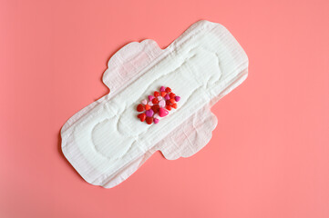 Fototapeta na wymiar women's menstrual sanitary pad or napkin for normal profusion of secretions with red and pink beads in the shape of hearts as an imitation of blood on pink background