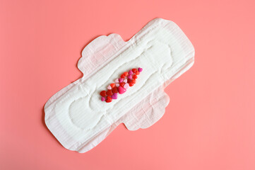 women's menstrual sanitary pad or napkin for normal profusion of secretions with red and pink beads in the shape of hearts as an imitation of blood on pink background