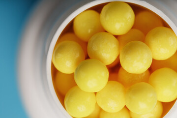 Vitamins of yellow color in the form of round dragees in a white jar on a blue background.