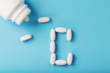 The letter of vitamin C in capsules pour out from the jar on a blue background.