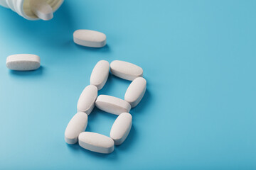 White capsules with vitamins in the form of B poured from a jar on a blue background