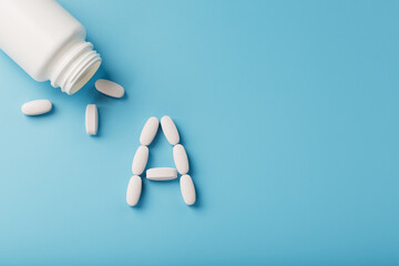 Vitamin A pills fell out of a white jar on a blue background.