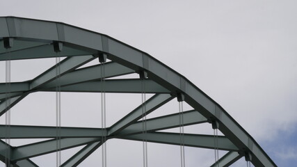 Suspension bridge with metal work and steel cables against a cloudy sky in mid afternoon day