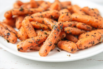 White plate with small peeled pieces of cooked baby carrot on white textured wooden table