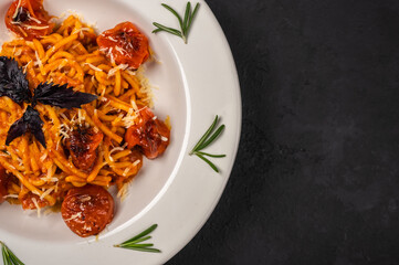 Close up pasta with cherry tomatoes, cheese and rosemary served on plate on dark textured background, selective focus, top view, copy space