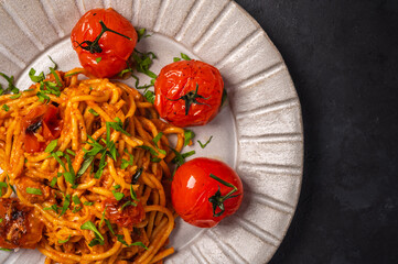 Close up pasta with baked cherry tomatoes, cheese and parsley on a dark textured background, selective focus, top view, copy space